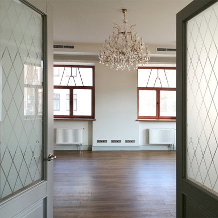 Wide reception hall with a crystal chandelier, hardwood floor and an open kitchen door