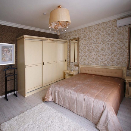 Bedroom with a cream built-in wardrobe, tufted headboard, and floral wallpaper