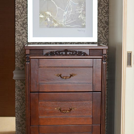 Carved wooden dresser with brass hardware beneath a framed abstract artwork