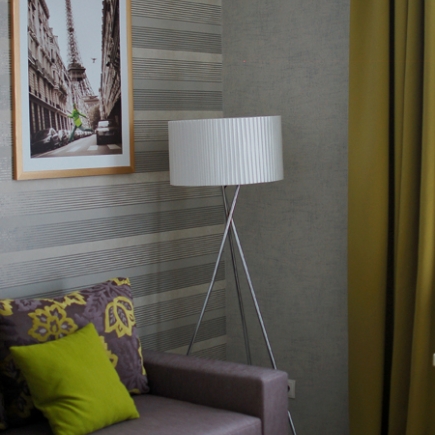 Close-up of a tripod floor lamp beside a Paris-print artwork and patterned throw pillows
