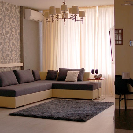 Living room with a gray-and-cream sectional sofa, ornate candelabra chandelier, and sheer curtains