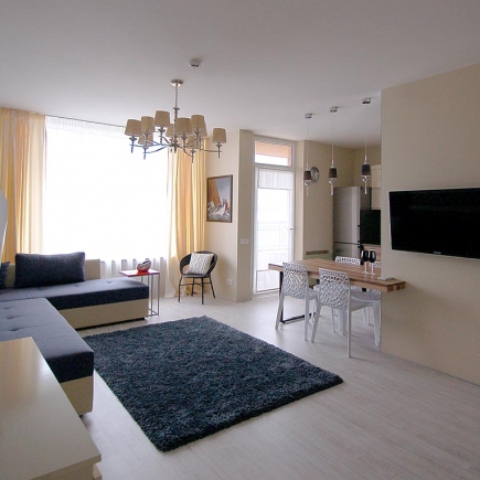 Open-plan living and dining room with a crystal chandelier, blue sectional sofa, and dark area rug