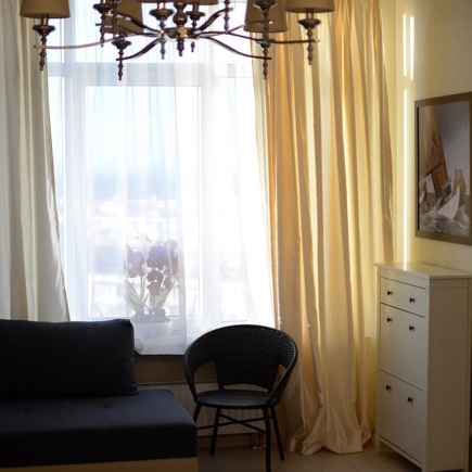 Reading nook with a dark sofa, wicker chair, and sheer curtains beside a large window