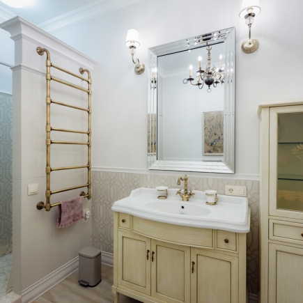 Bathroom with a brass heated towel rail, beveled mirror, and cream vanity cabinet