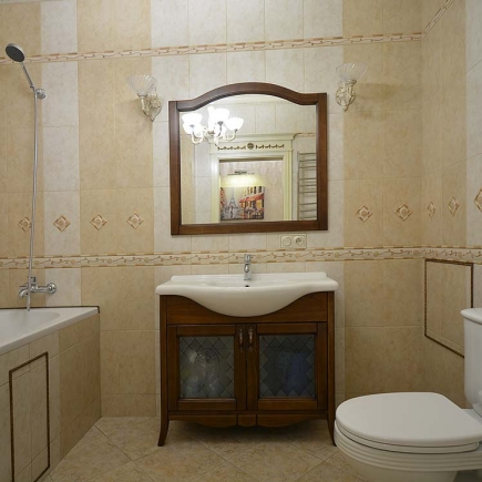 Bathroom with mosaic tile trim, a wood-framed mirror, and a wall-mounted crystal sconce