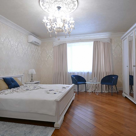 Bedroom with damask wallpaper, a crystal chandelier, navy accent chairs, and wood flooring