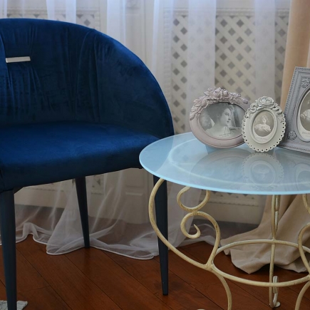 Corner with a navy velvet accent chair beside a wrought-iron side table with framed photos