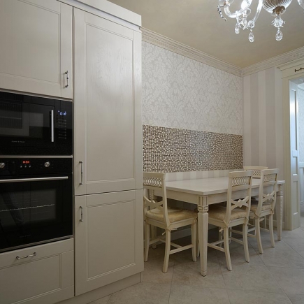 Kitchen dining nook with a damask accent wall, built-in ovens, and upholstered chairs