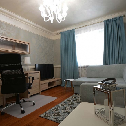 Living room with damask wallpaper, teal curtains, a gray sectional sofa, and a crystal chandelier
