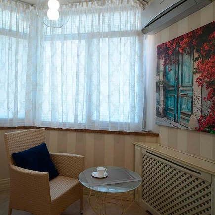Reading nook with a wicker armchair, sheer curtains, and a framed photograph of a blue door