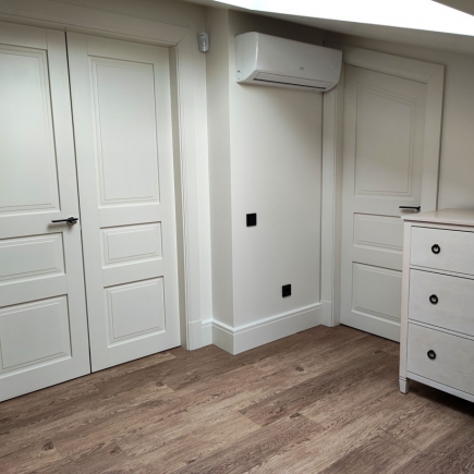 Attic bedroom closet doors beside a wall-mounted air conditioning unit and dresser