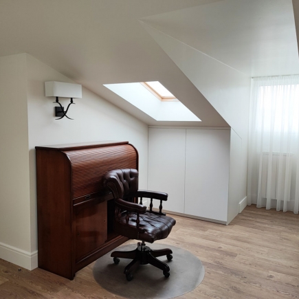Attic study nook with a leather rolltop desk and chair beneath a skylight