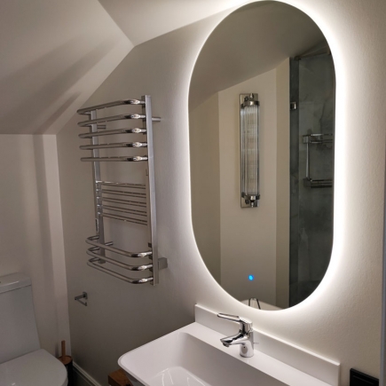 Backlit oval mirror above a bathroom vanity beside a heated towel rail
