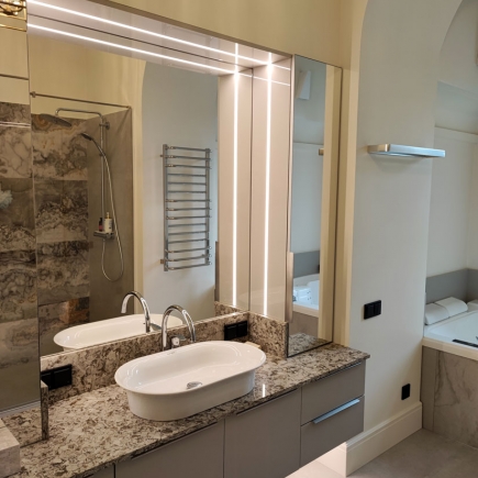 Bathroom vanity with dual sinks, marble countertop, backlit mirror, and heated towel rail