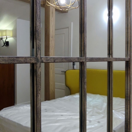 Bedroom with mustard-yellow upholstered headboard seen through an antique window frame
