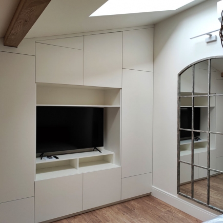 Built-in wall unit with wall-mounted TV beneath a skylight, beside a large arched mirror