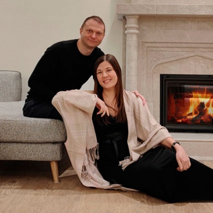 Couple relaxing on the floor beside a sofa in front of a lit marble fireplace