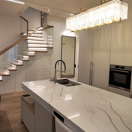 Curved staircase beside a marble kitchen island with crystal chandelier and mirrored wall