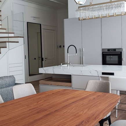 Dining table with wooden top beside the kitchen island, glass staircase, and mirrored wall