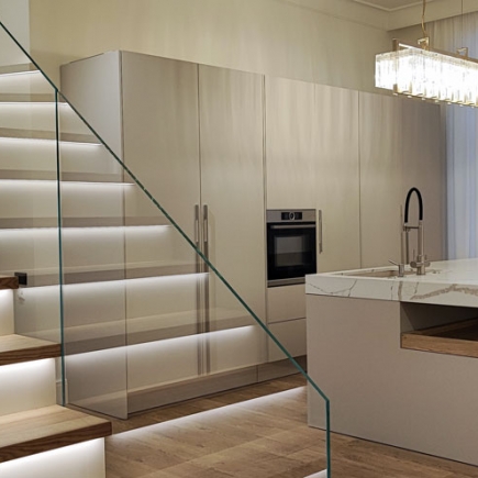 Floating staircase beside built-in cabinetry with wall-mounted oven and integrated LED toe-kick lighting