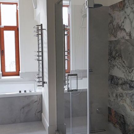 Glass-enclosed walk-in shower beside a marble-clad soaking tub