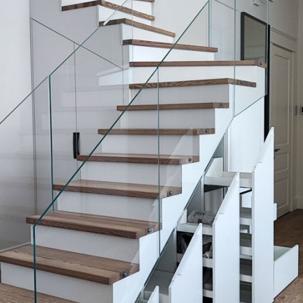 Glass-railed staircase with wood treads beside built-in under-stair drawers