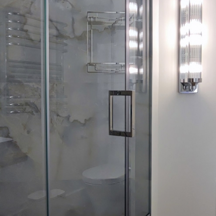 Glass shower enclosure beside a wall sconce and marble-tiled wall