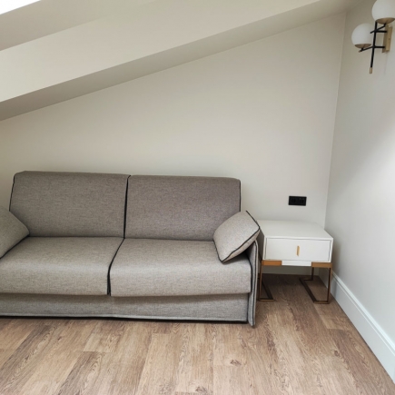 Gray sofa bed beside a built-in nightstand in an attic guest room