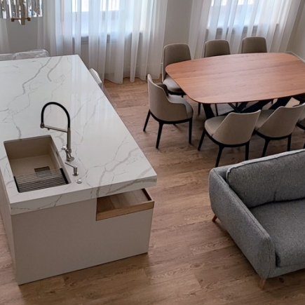 Kitchen island with marble waterfall countertop beside a dining table and gray upholstered sofa