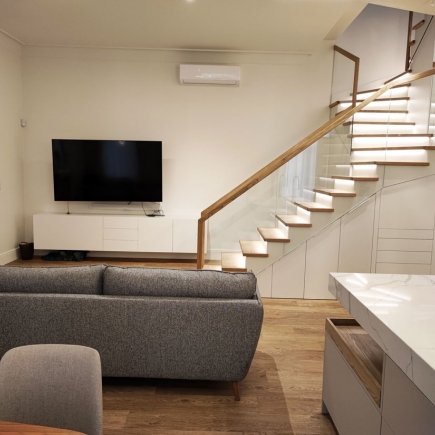 Living room with wall-mounted TV, floating media console, and wood-and-glass staircase