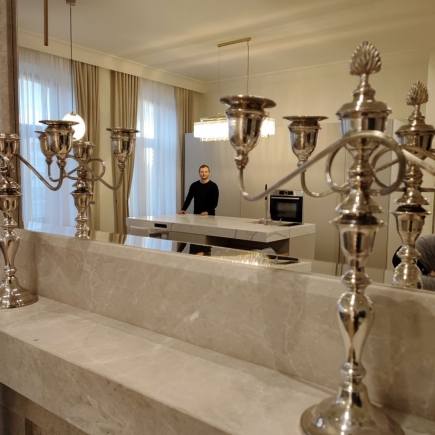 Marble bench beside silver candelabra with a figure visible at the kitchen island beyond