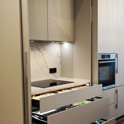 Open kitchen cabinet with induction cooktop, marble backsplash, and pull-out drawer organizers