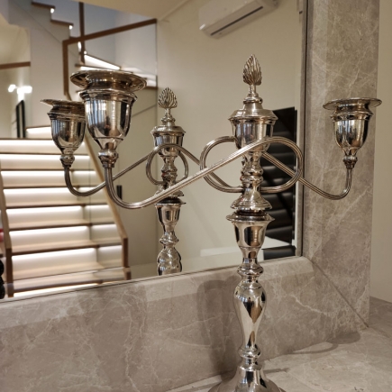 Silver candelabra on the marble fireplace mantel with staircase reflected in the mirror