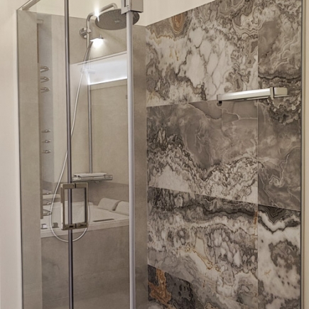Walk-in shower with handheld showerhead beside a dramatic gold-veined marble accent wall