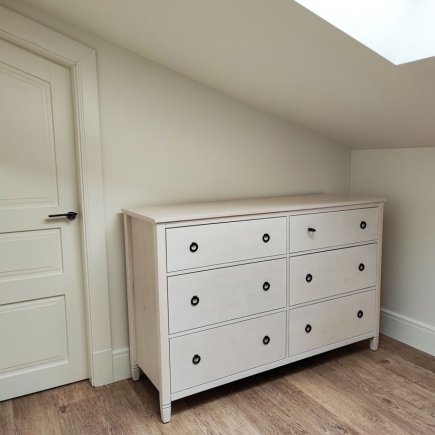 White dresser with round pulls positioned beneath a sloped attic ceiling