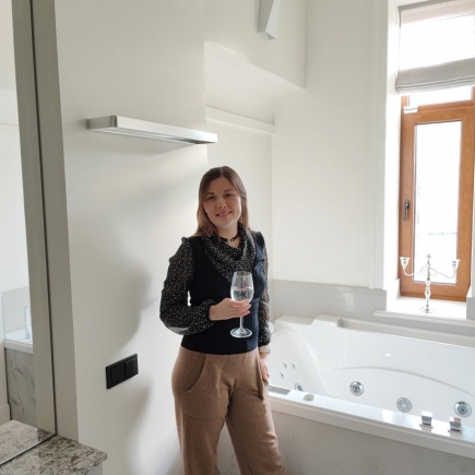 Woman holding a glass of wine beside a whirlpool tub and wood-framed window