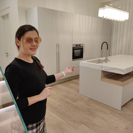 Woman standing beside a minimalist kitchen island with marble waterfall countertop and glass stair rail