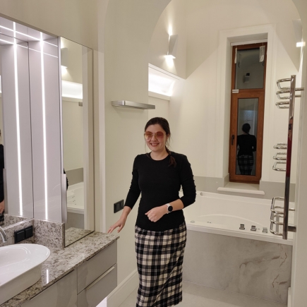 Woman standing in a marble bathroom beside a soaking tub and arched window