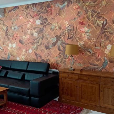 Black leather sofa corner against the bird-and-floral wallpaper and wooden sideboard with brass lamps