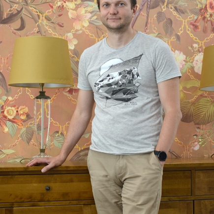 Client standing beside the wooden sideboard and table lamp against the floral wallpaper