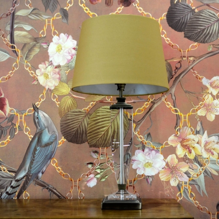 Close-up of a crystal table lamp with a mustard-yellow shade against the bird-and-floral wallpaper