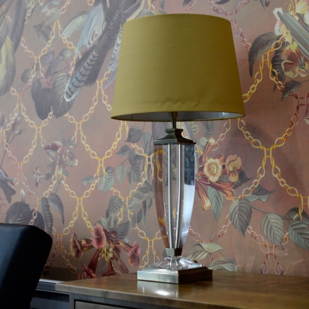 Crystal table lamp with mustard shade on the wooden sideboard against the floral wallpaper