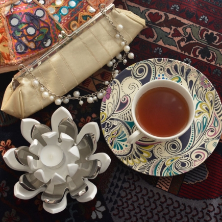 Flat-lay of a beaded clutch bag, pearl necklace, and a cup of tea on a patterned textile