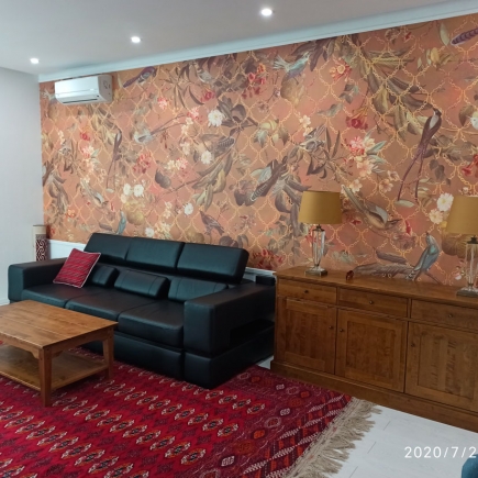 Living room with black leather sofa, red accent pillow, and wooden sideboard beneath the statement wallpaper