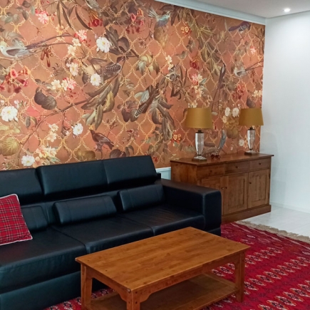 Wide view of the living room with black leather sofa, wooden sideboard, and patterned red rug