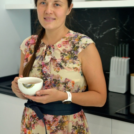 Woman in a floral dress holding a teacup in the kitchen with a dark marble backsplash
