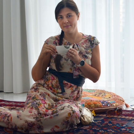 Woman in a floral dress sitting cross-legged on a patterned rug holding a teacup