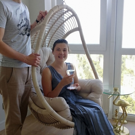 Couple posing beside the rattan hanging chair, she holding a glass of wine