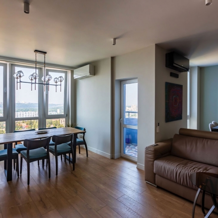 Dining and living area with floor-to-ceiling windows, wood dining table, and city skyline view