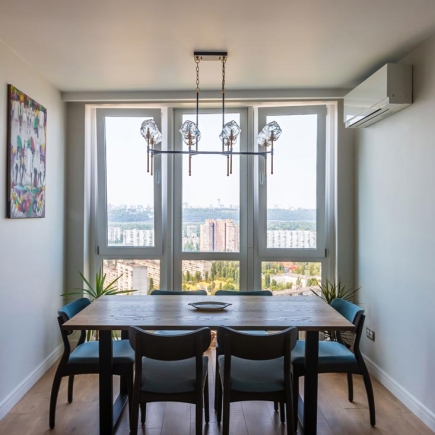 Dining table beneath a statement chandelier with floor-to-ceiling windows overlooking the city